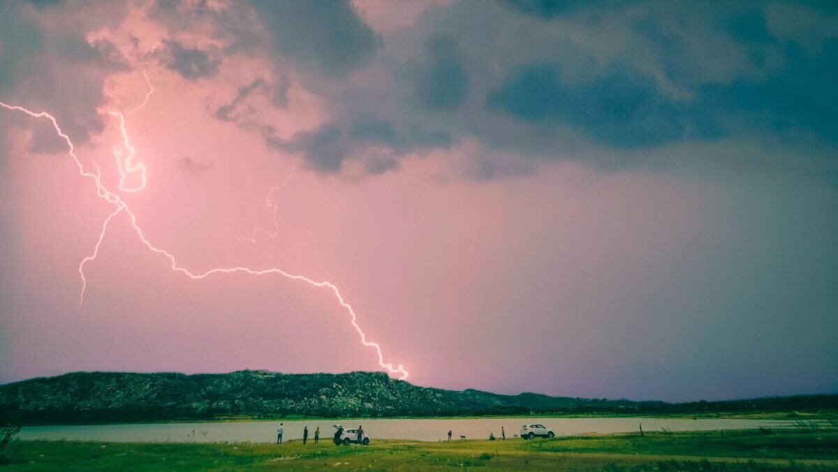 Bolt of lightning streaking across a rosy sky filled with dark, billowing storm clouds